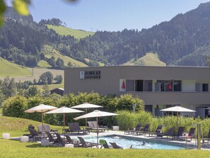 A modern building with a sign for 'TAUERN RESIDENCE' and a pool area with lounge chairs and umbrellas. - Apartment in Radstadt With Swimming Pool (Radstadt)