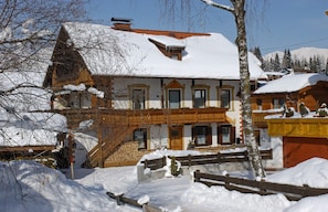 Ein traditionelles Holzhaus mit geneigtem Dach, einer Holztreppe und einem schneebedeckten Hof.