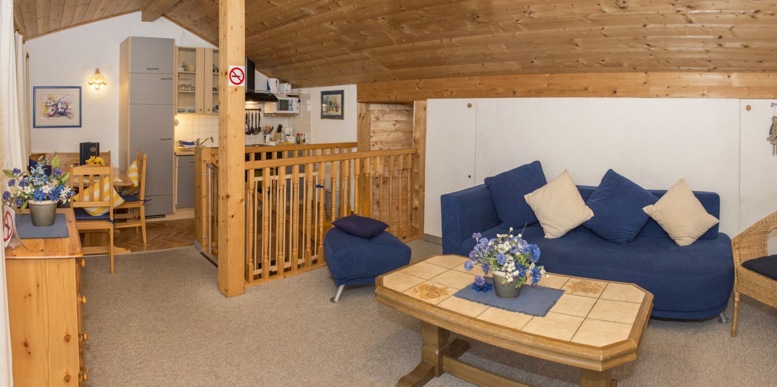 A cozy room with a blue sofa, wooden furniture, and a kitchen area in the background.