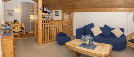 A cozy room with a blue sofa, wooden furniture, and a kitchen area in the background.