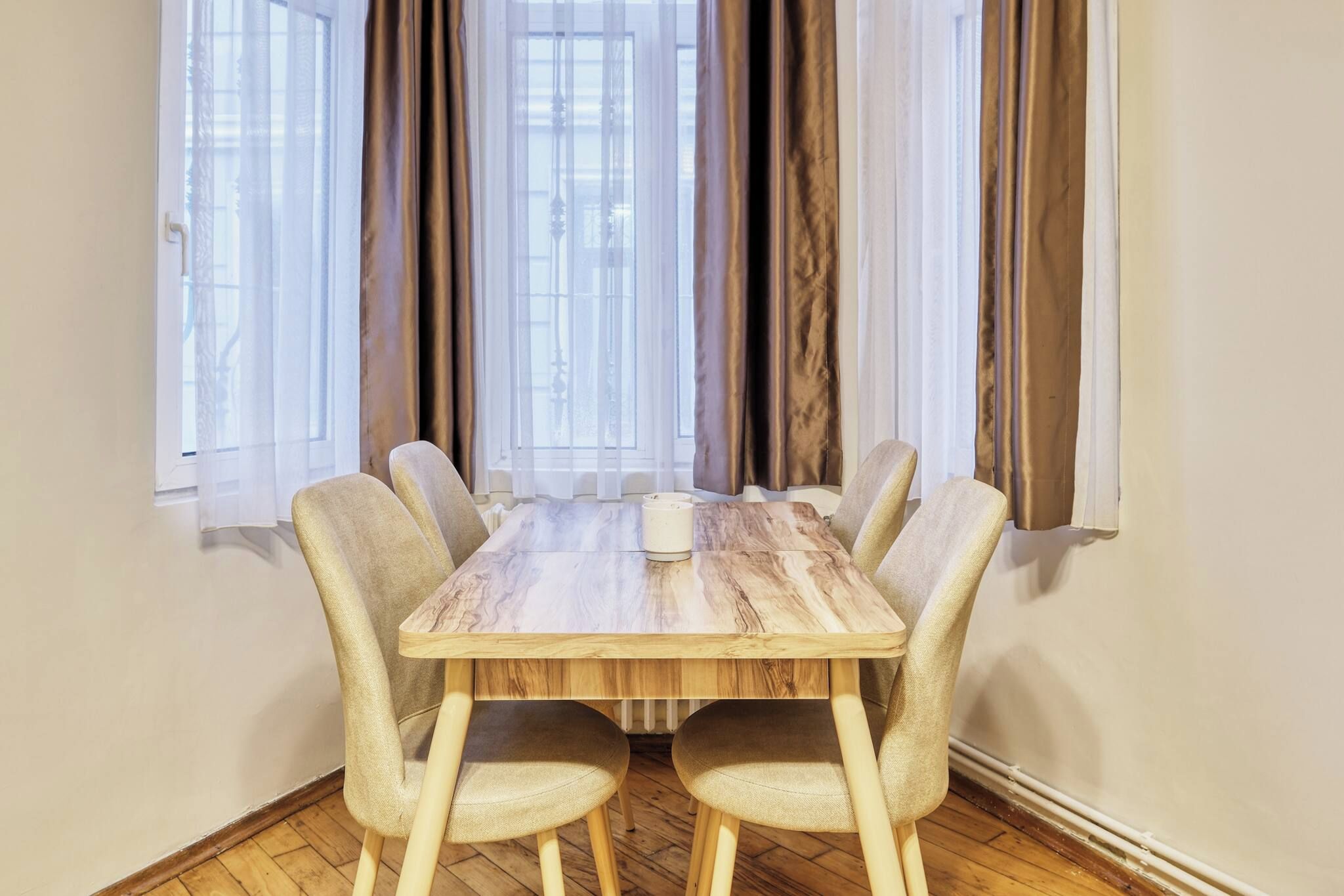 A dining table with six chairs, a white tablecloth, and a window with curtains.