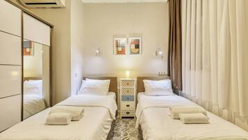 A hotel room with two beds, a bedside table with a lamp, a wall-mounted air conditioner, and a mirror.