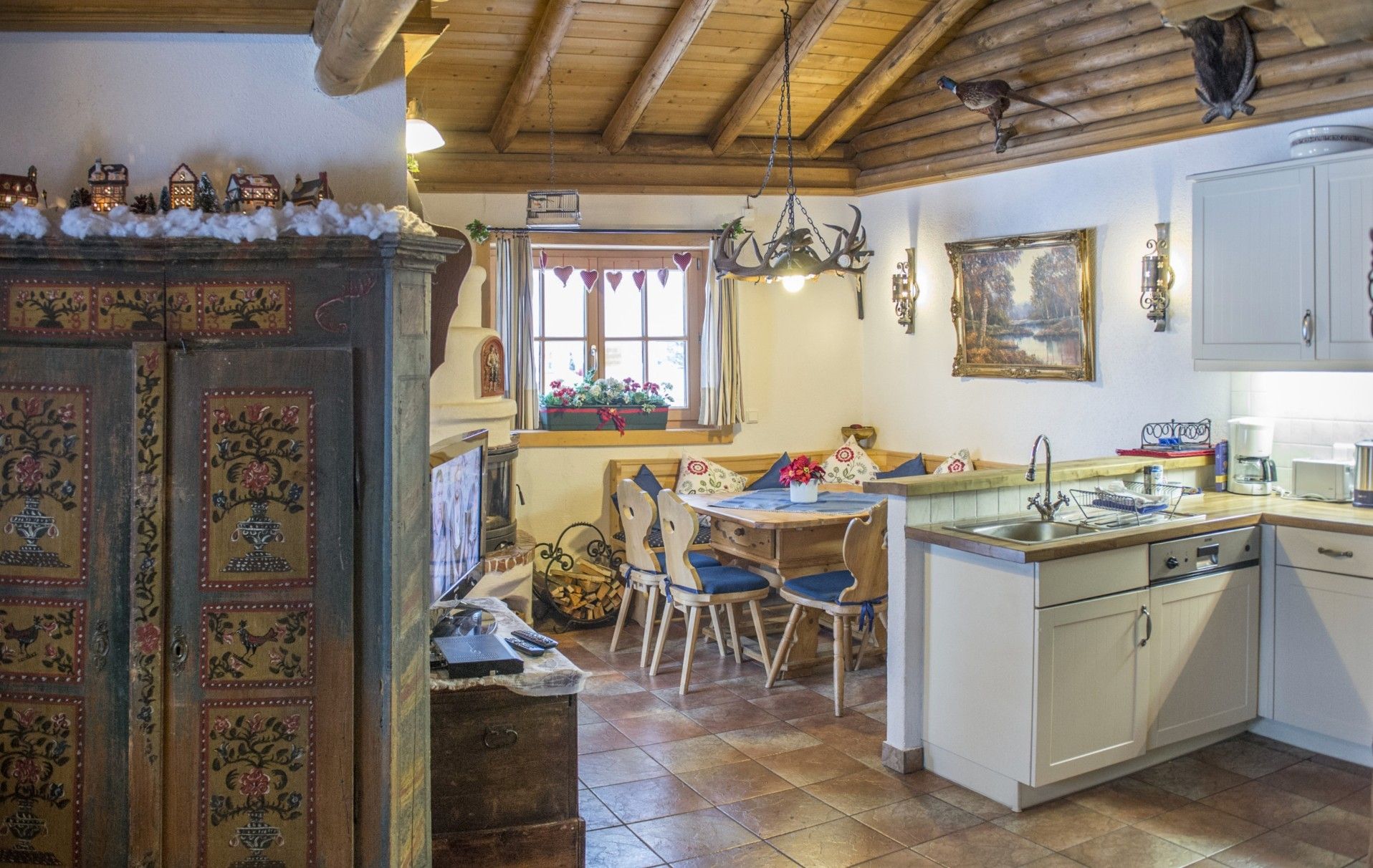 Cozinha rústica com armários de madeira, área de jantar com mesa e cadeiras, e lareira com manto decorativo.