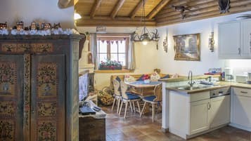 Cozinha rústica com armários de madeira, área de jantar com mesa e cadeiras, e lareira com manto decorativo.