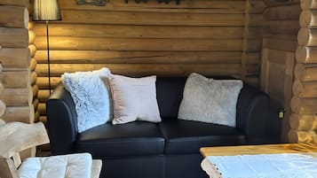 A log cabin interior with a black leather sofa, a wooden table, and a lamp.