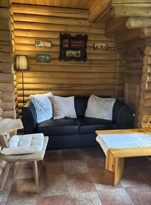 A log cabin interior with a black leather sofa, a wooden table, and a lamp. - Blockhaus Schwalbennest: Mountain Views, Private Garden & WiFi in Seefeld (Seefeld in Tirol)