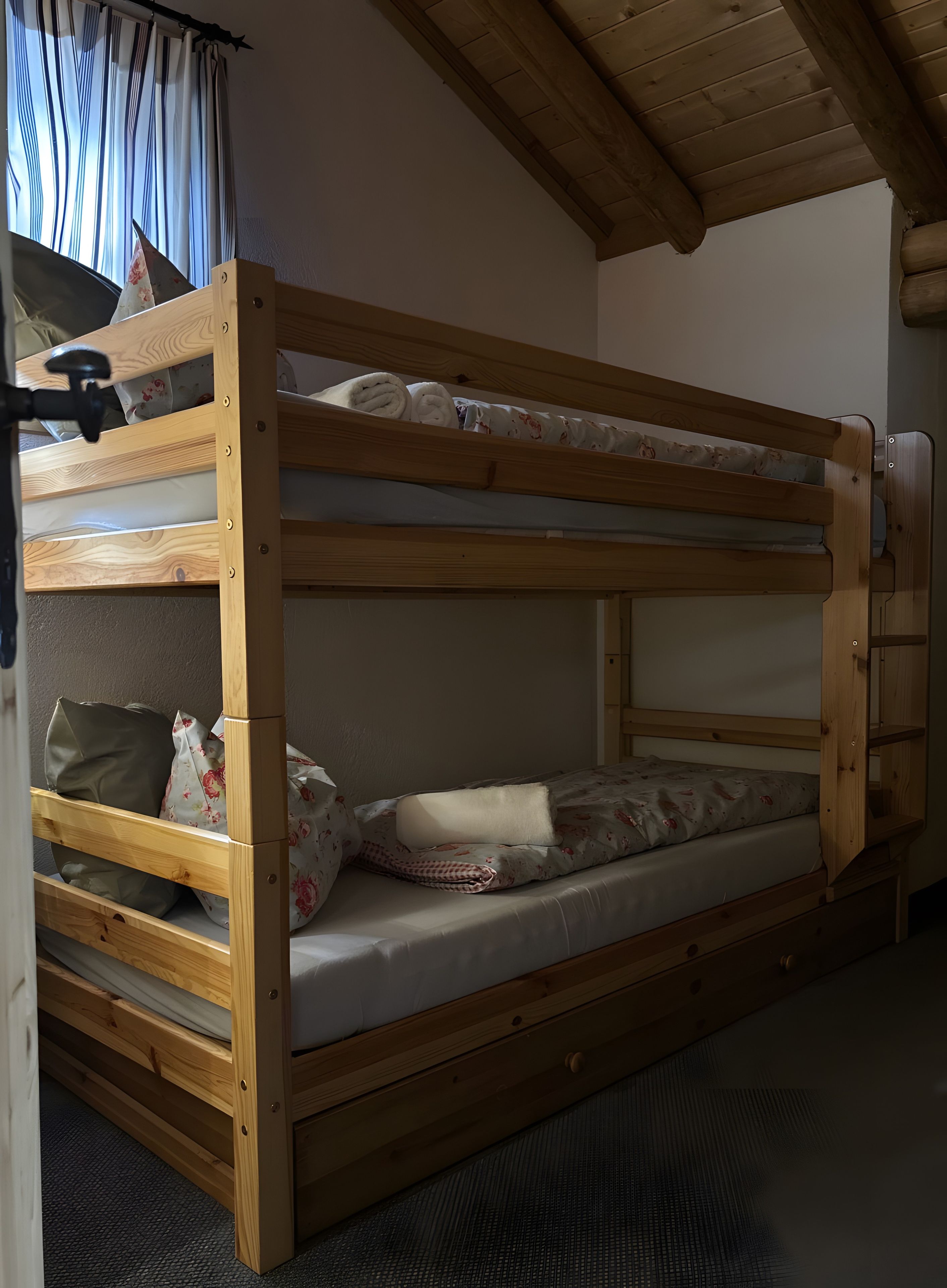 Ein Stockbett mit Holzrahmen, einer Matratze, Kissen und einer kleinen Schublade.
