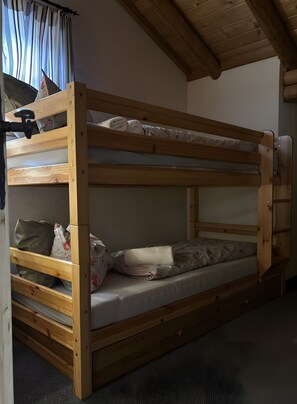 Ein Stockbett mit Holzrahmen, einer Matratze, Kissen und einer kleinen Schublade.