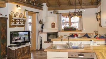 A cozy kitchen with a wooden ceiling, a television on a cabinet, a sink, and a window with a view.