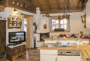 A cozy kitchen with a wooden ceiling, a television on a cabinet, a sink, and a window with a view.