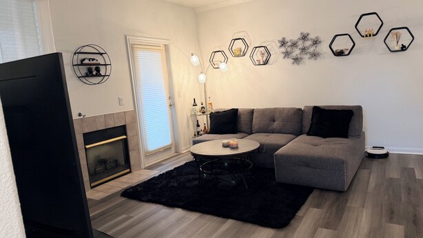 Een moderne woonkamer met een grijze bank, een zwart tapijt, een ronde salontafel en een open haard.