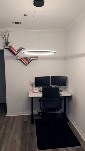 A modern office space with a desk, two monitors, a chair, a black rug, and a unique ceiling light fixture. - Modern Furnished Retreat Cozy & Convenient (Castle Rock)