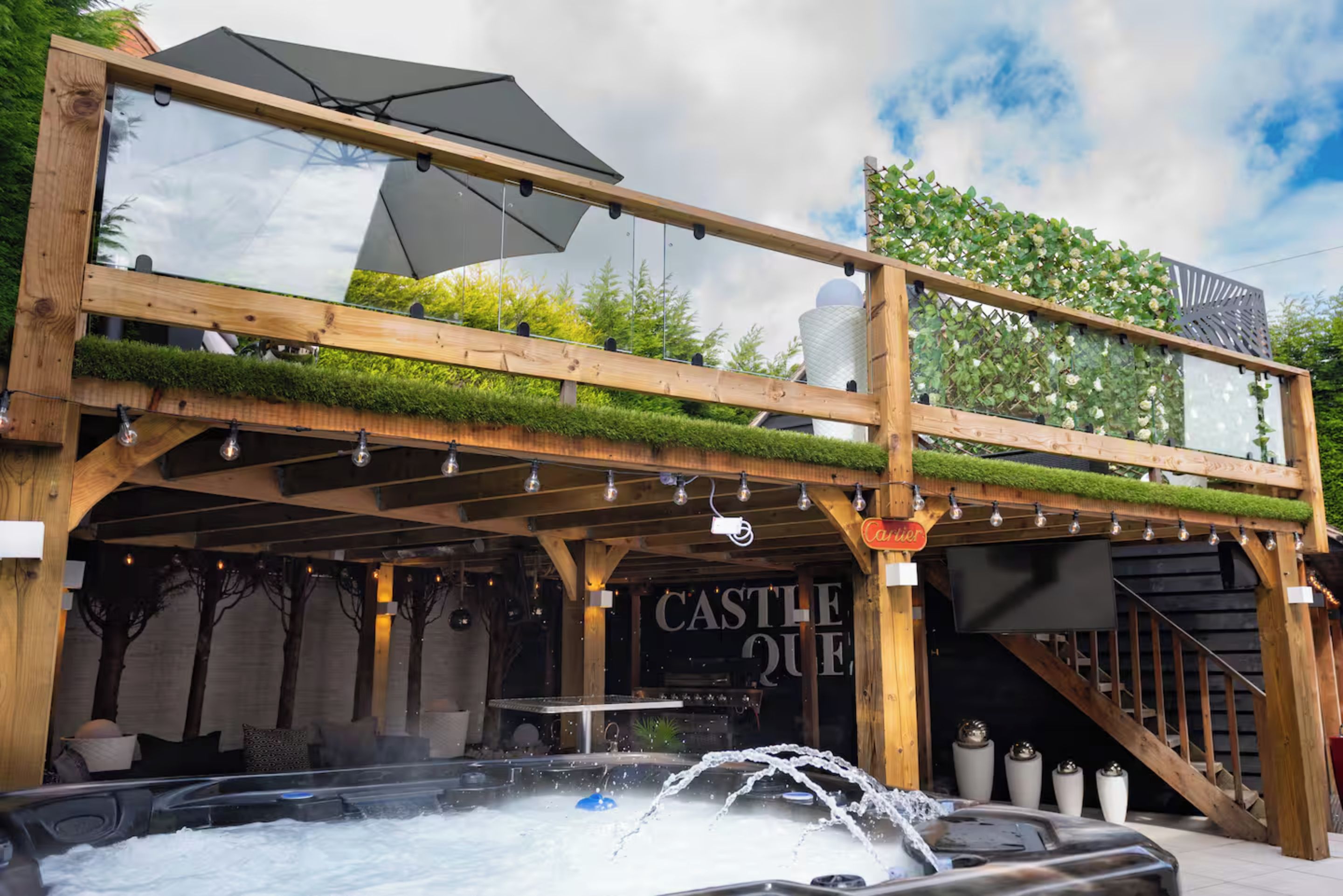 A wooden structure with a hot tub, a sign reading 'CASTLE QUE,' and a staircase leading to an upper level.