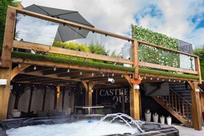 Estructura de madera con un jacuzzi, un letrero que dice 'CASTLE QUE' y una escalera que lleva a un nivel superior.