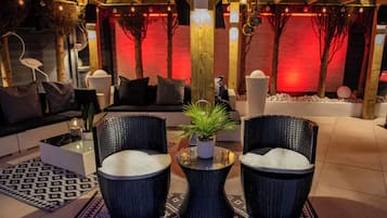 Un'area lounge moderna con un divano, due poltrone in vimini, un tavolino con una pianta e illuminazione decorativa.