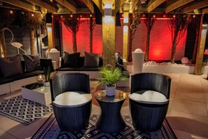 A modern lounge area with a sofa, two wicker chairs, a small table with a plant, and decorative lighting.