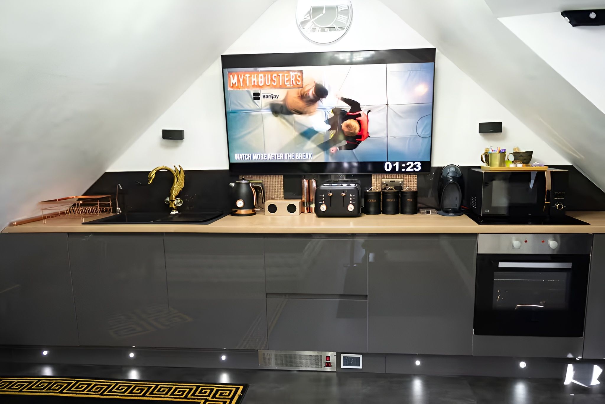 Una cocina moderna con un televisor de pantalla plana mostrando un programa, una cafetera, un tostador y un microondas.