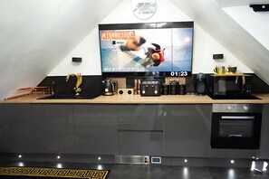 Una cocina moderna con un televisor de pantalla plana mostrando un programa, una cafetera, un tostador y un microondas.