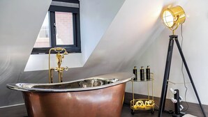 A modern bathroom with a freestanding bathtub, a window with a black frame, and a floor lamp.