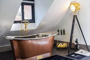 Un baño moderno con una bañera independiente, un ventanal con marco negro y una lámpara de pie.
