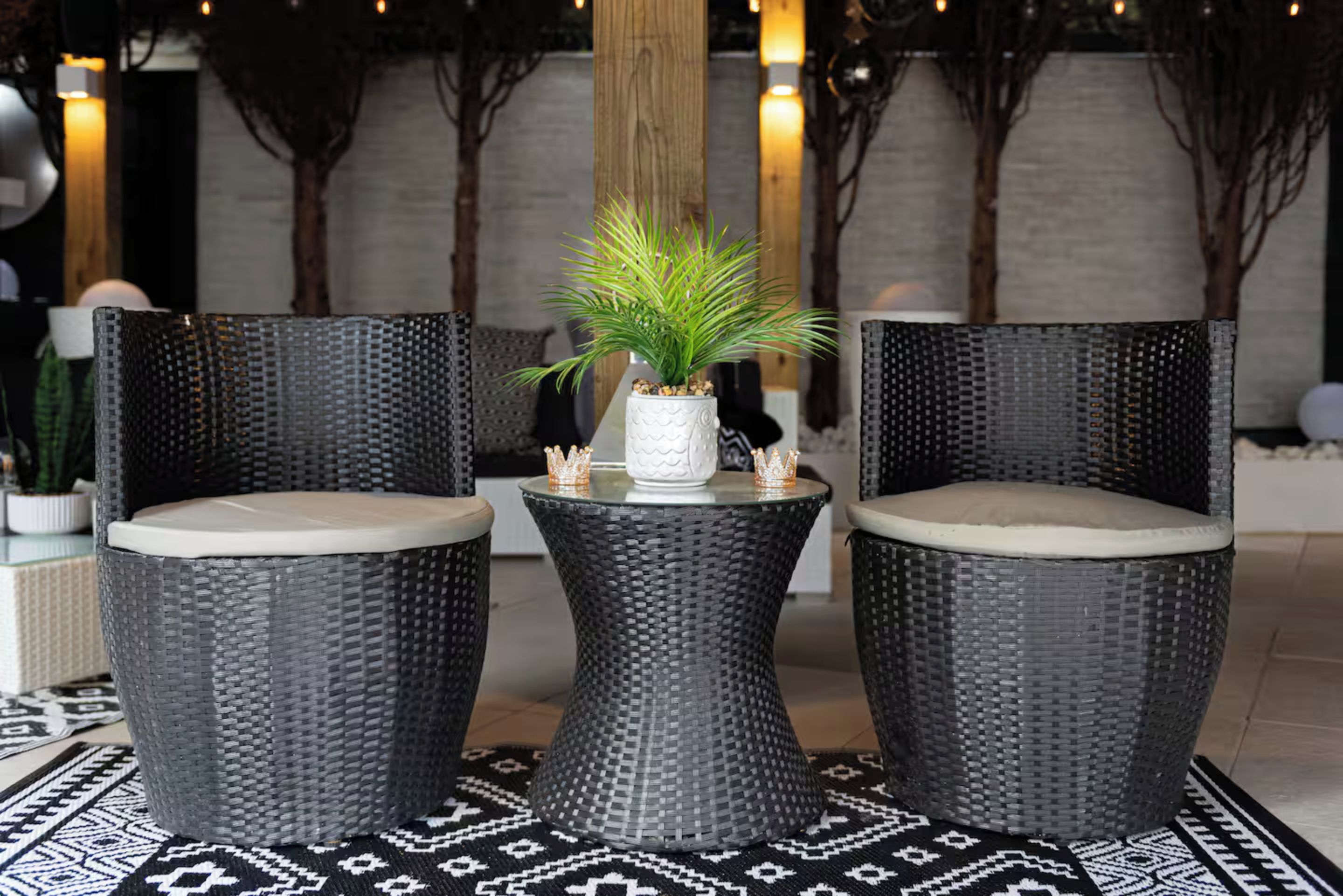 A seating area with two wicker chairs and a small table, each with a cushion. A potted plant is on the table.