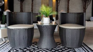 A seating area with two wicker chairs and a small table, each with a cushion. A potted plant is on the table.