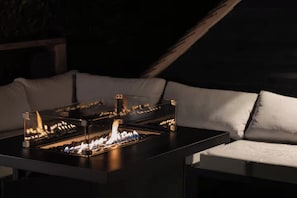 Un área de estar moderna al aire libre con una mesa de vidrio y una chimenea integrada.