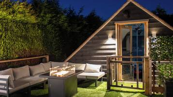A cozy outdoor seating area with a fire feature, a wooden deck, and a glass-enclosed structure.