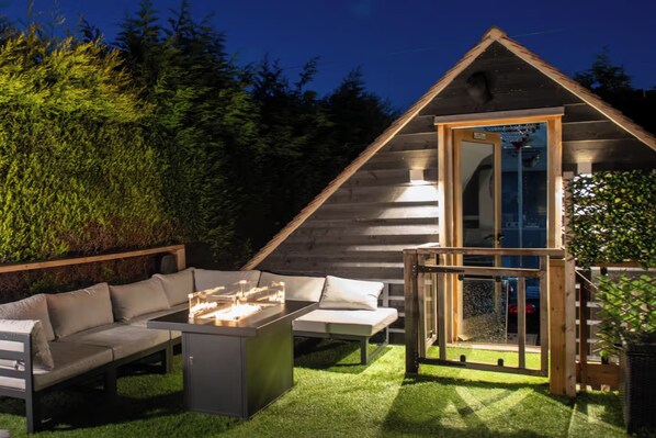 A cozy outdoor seating area with a fire feature, a wooden deck, and a glass-enclosed structure.