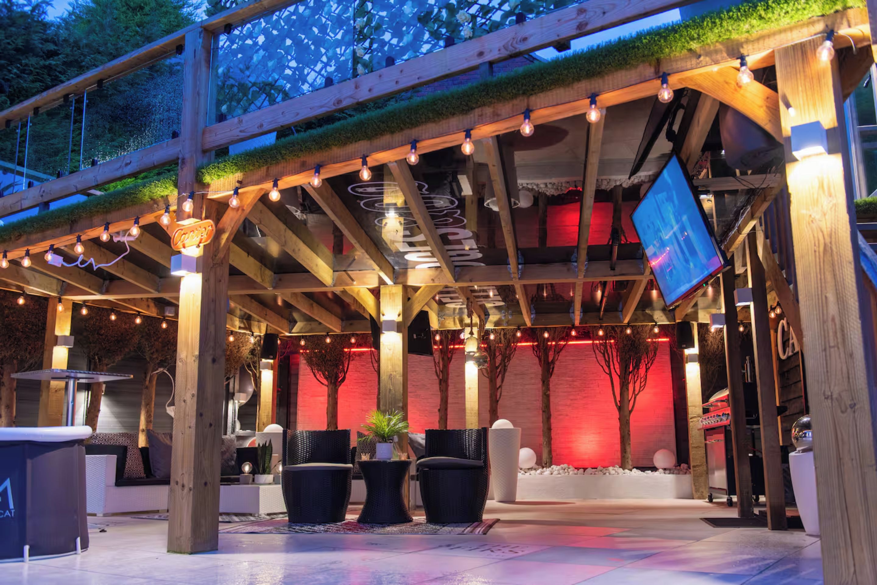 An outdoor seating area with wooden beams, string lights, and a flat-screen TV.