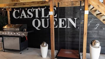 Un área de cocina con estufa de acero inoxidable, una pared negra con las palabras 'CASTLE QUEEN' en letras blancas, y dos macetas blancas con objetos esféricos.