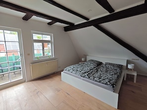 A bedroom with a sloped ceiling, a bed with patterned bedding, a radiator, and a window with a view of buildings. - Geräumige Ferienwohnung am Schönbuchrand für Familien & Gruppen bis zu 7 Pers. (Ammerbuch)