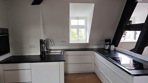 Eine moderne Küche mit weißen Schränken, einer schwarzen Arbeitsplatte, einem eingebauten Ofen und einem Fenster mit Blick auf Grünflächen.