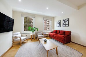 Ein Wohnzimmer mit einem roten Sofa, zwei Sesseln, einem Couchtisch und einem an der Wand befestigten Fernseher.
