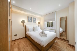 Ein Schlafzimmer mit einem hölzernen Bett, weißer Bettwäsche, zwei Wandlampen und einem großen Fenster.