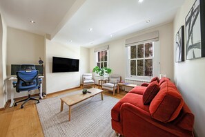 Ein modernes Wohnzimmer mit einem roten Sofa, einem blauen Bürostuhl, einem Holztisch und einem an der Wand befestigten Fernseher.