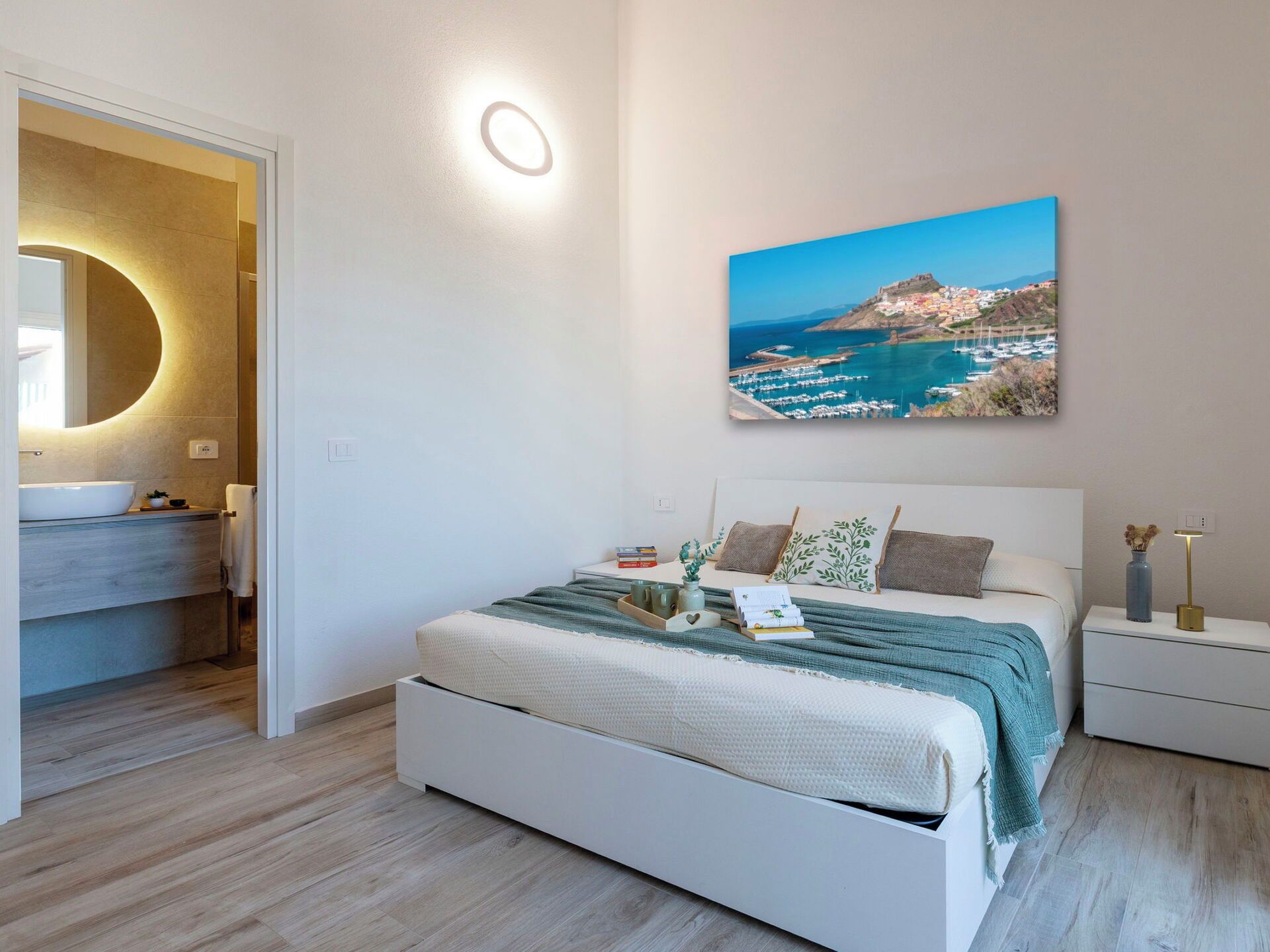 Ein Schlafzimmer mit Bett, Nachttischen, einem Wandbild und einem Badezimmer mit Badewanne und Spiegel.