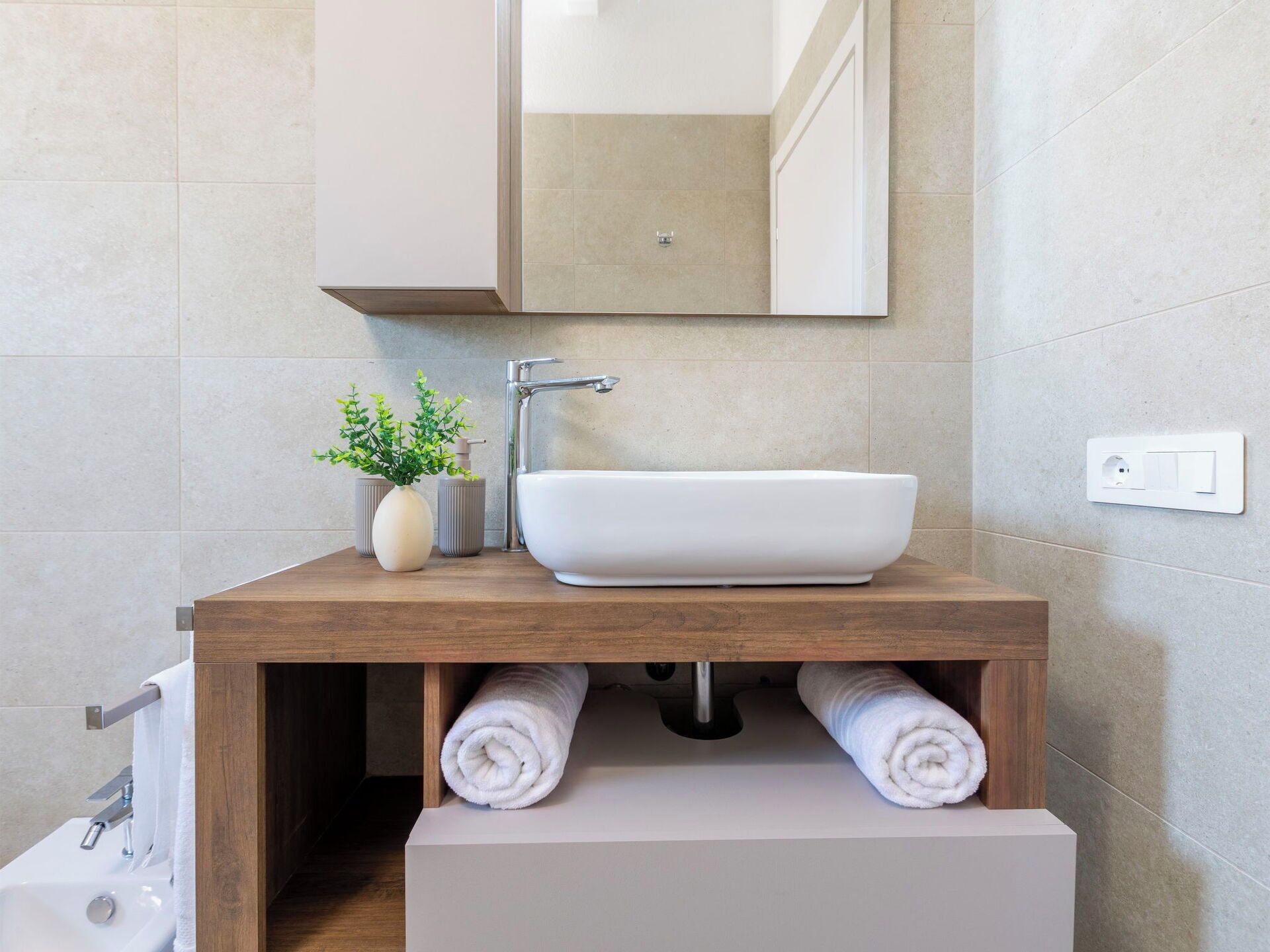 Een badkamer met een houten wastafelmeubel, een witte wasbak en een spiegel erboven.
