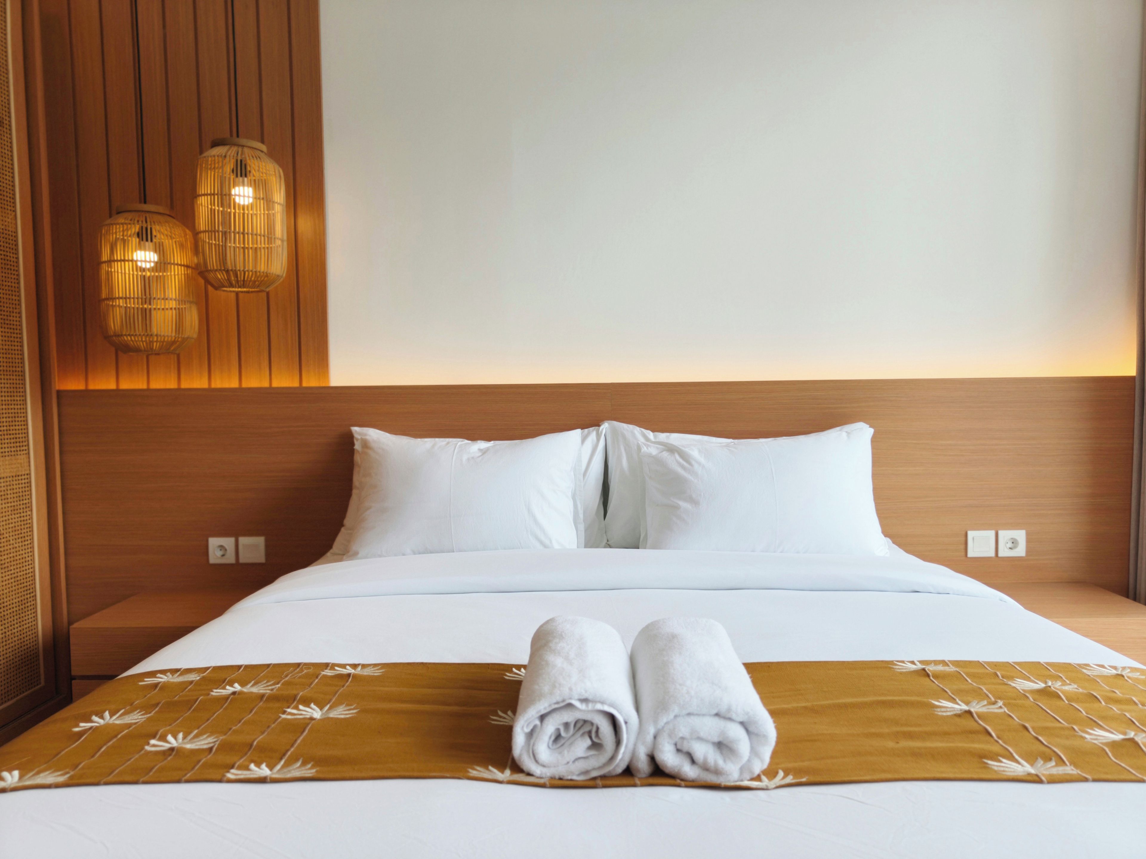 Un lit bien fait, avec des draps blancs et deux serviettes enroulées posées sur une couverture marron.