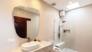 Uma casa de banho moderna com um espelho oval grande, uma sanita branca, uma pia e uma área de duche com parede de vidro.
