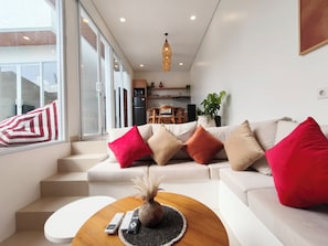 A modern living room with a sofa, a coffee table, and a view of the kitchen. - Samanaya Villa (Badung)