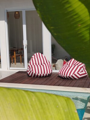 A poolside area with two bean bags, a sliding glass door, and a view of a dining area. - Samanaya Villa (Badung)