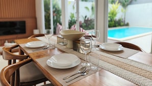 Mesa de jantar posta com pratos, copos e talheres, com vista para uma piscina e vegetação.