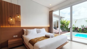 Quarto de hotel moderno com uma cama grande, cabeceira de madeira, mesinha de cabeceira e vista para uma piscina através de grandes portas de vidro.