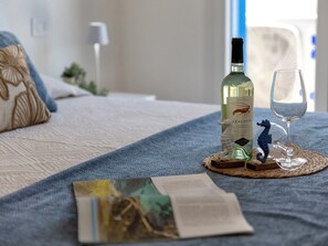 Una cama con un libro, una botella de vermut Aragosta y un vaso sobre un posavasos tejido.