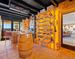 Ein Weinkeller mit Holzeinlagen und Fässern, eine Bar mit Hockern sowie eine gemütliche Sitzecke mit Sofa und Couchtisch.