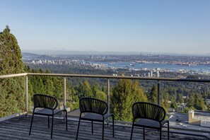 A balcony with three chairs overlooking a cityscape with a bridge and a mountain in the distance.