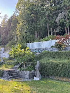 Ein Garten mit einer Steintreppe, die zu einem weißen Zaun führt, umgeben von dichtem Grün und Bäumen.