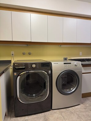 A laundry area with two washing machines, one black and one silver, and white cabinets above.