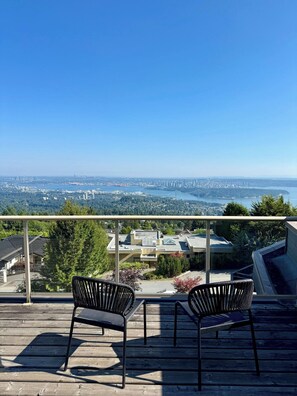 A balcony with two chairs overlooking a cityscape and a bridge.